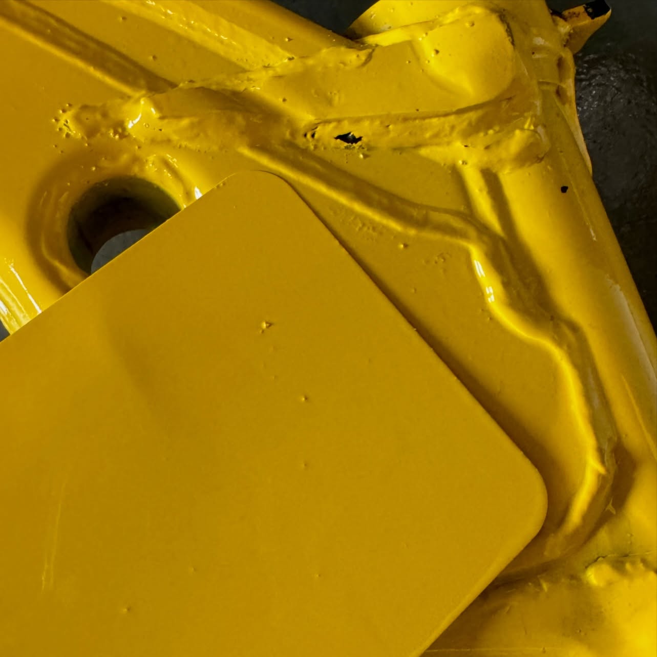 Yellow painted metal component beside a matching yellow test panel